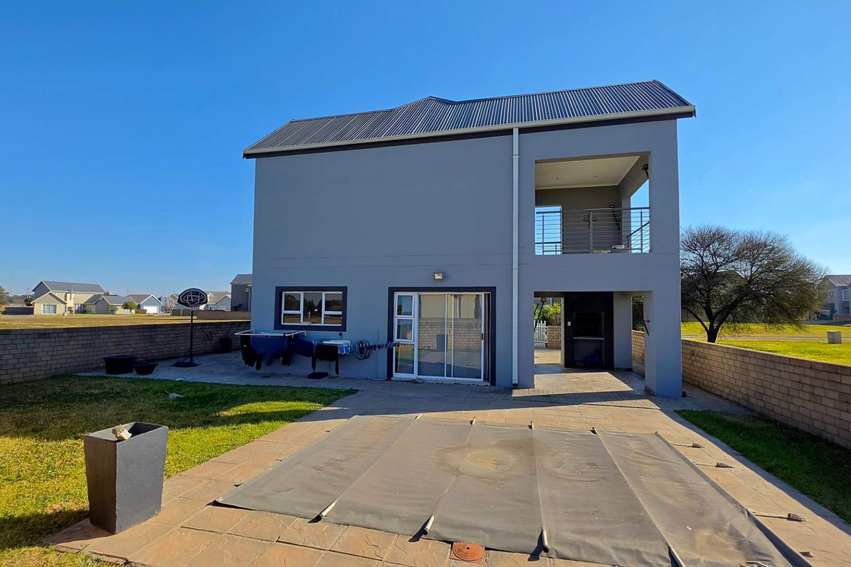 Rear view of a two-story townhouse featuring a paved patio, swimming pool with cover, and an upper-level balcony.