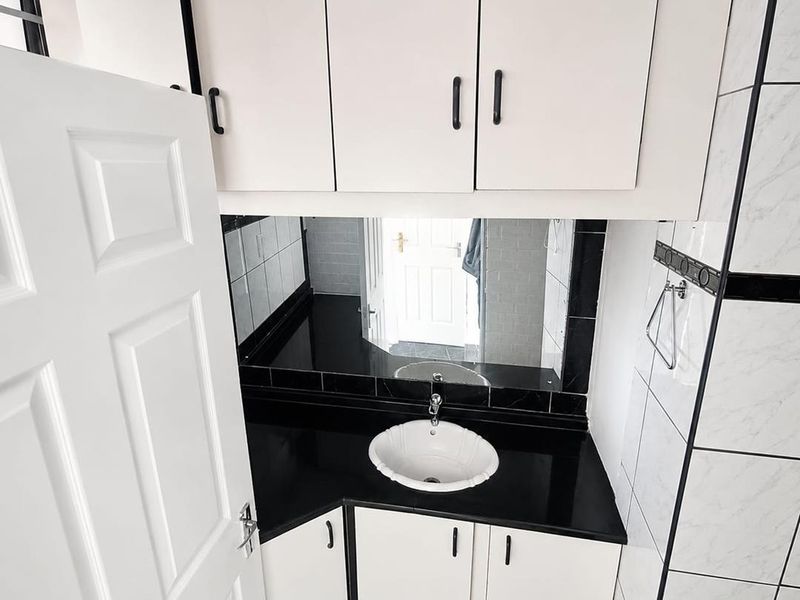 A compact bathroom featuring a black granite vanity top, white cabinetry, and monochrome tiled finishes.