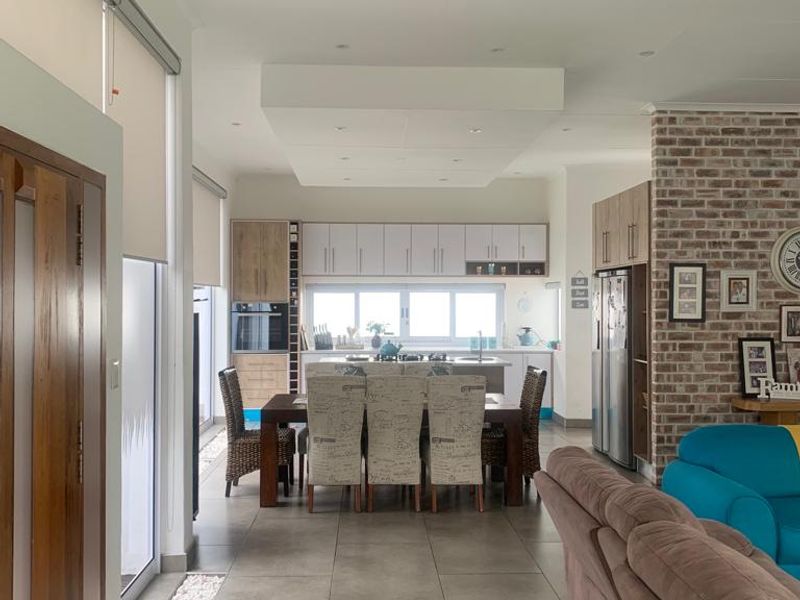 Spacious open-plan living and dining area featuring modern tiled floors, an exposed brick feature wall, and a contemporary kitchen with integrated appliances.