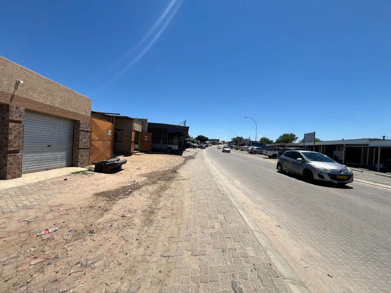 A street-level view of the property frontage showing the paved sidewalk, road access, and adjacent commercial or residential building structures.