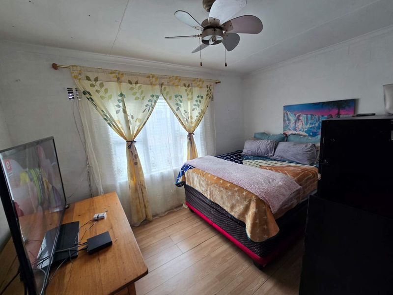 A bedroom featuring laminate flooring and a ceiling fan, currently showing signs of wear including wall and ceiling imperfections.