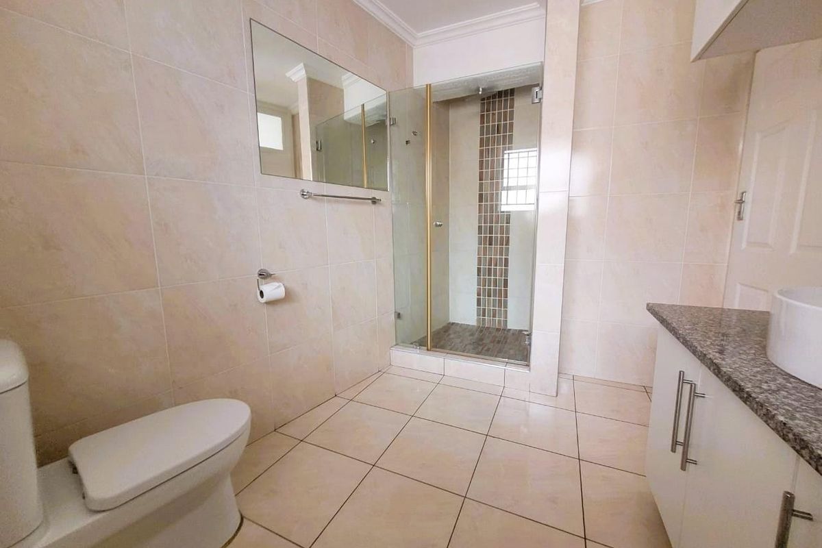 A well-maintained bathroom featuring a glass-enclosed shower, tiled walls and flooring, a vanity with a granite countertop, and a wall-mounted mirror.