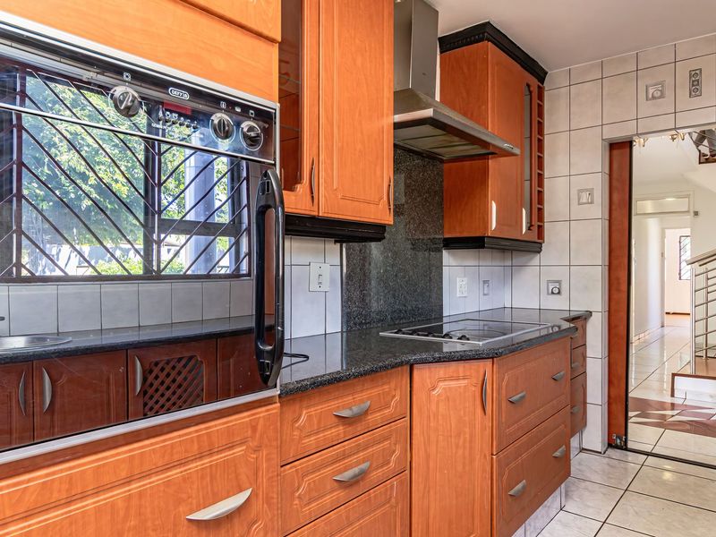 A functional kitchen featuring wooden cabinetry, granite countertops, a built-in oven, and a stainless steel extractor fan, with tiled finishes throughout.