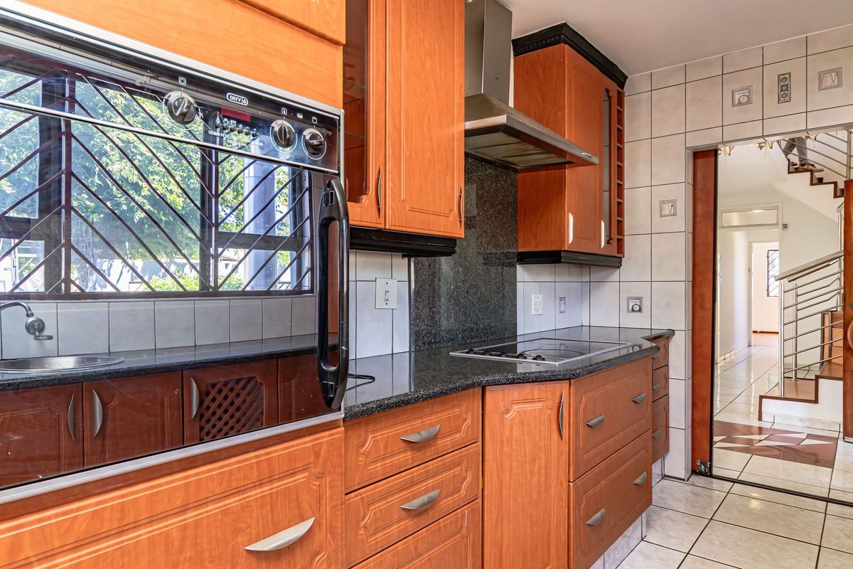 A functional kitchen featuring wooden cabinetry, granite countertops, a built-in oven, and a stainless steel extractor fan, with tiled finishes throughout.