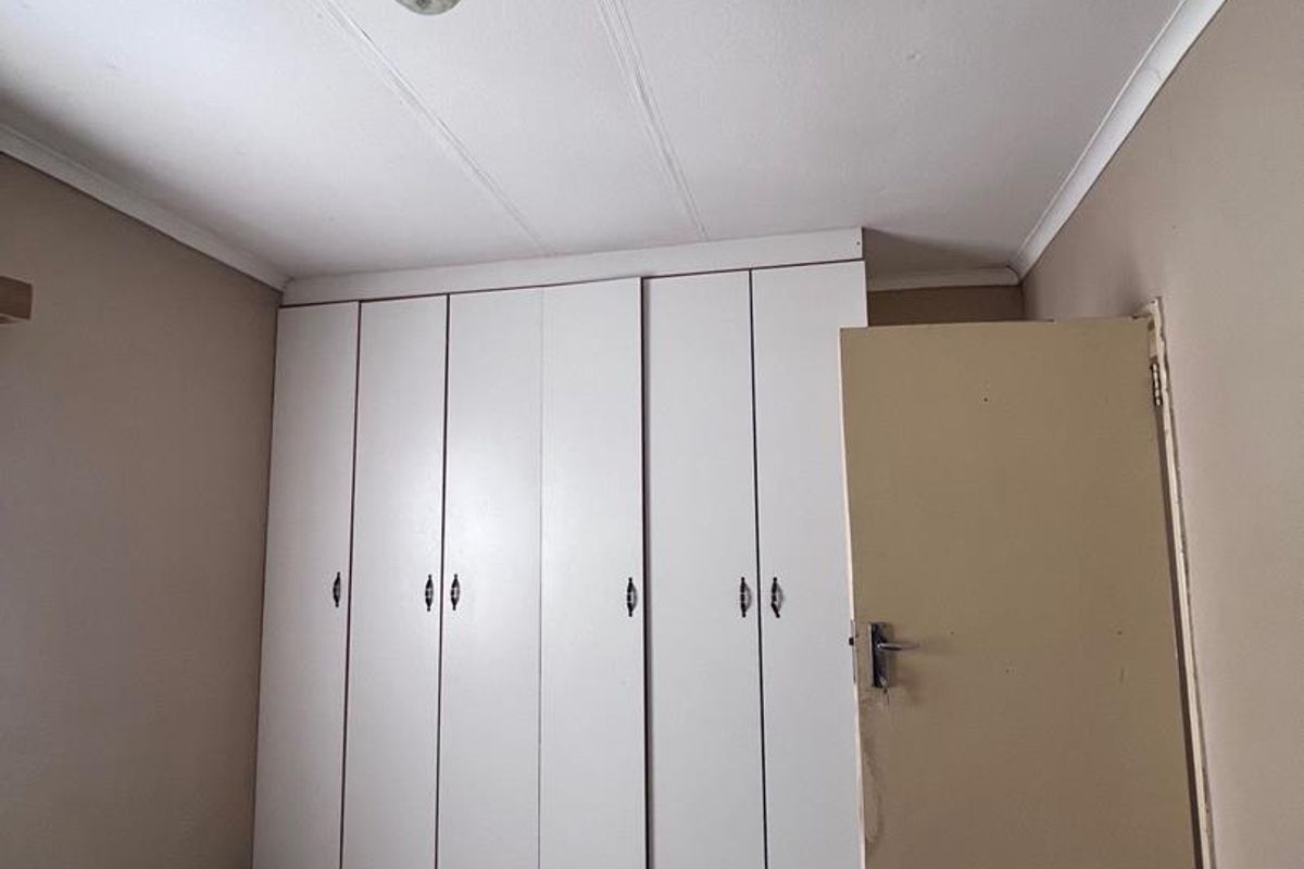 A vacant bedroom featuring built-in white cupboards, tiled flooring, and neutral wall tones, offering a blank canvas for potential updates.