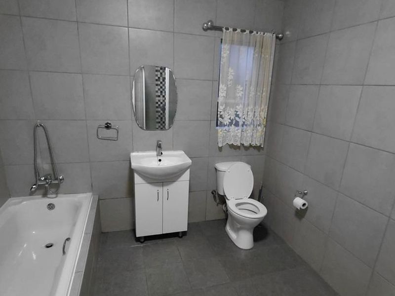 A functional bathroom featuring full-height wall tiling, a built-in bathtub, a vanity cabinet with a basin, and a standard toilet.