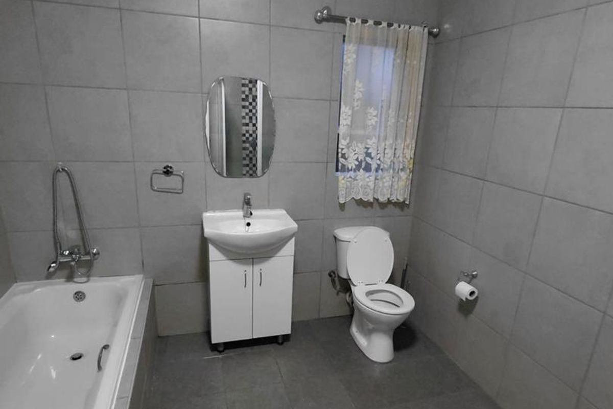 A functional bathroom featuring full-height wall tiling, a built-in bathtub, a vanity cabinet with a basin, and a standard toilet.