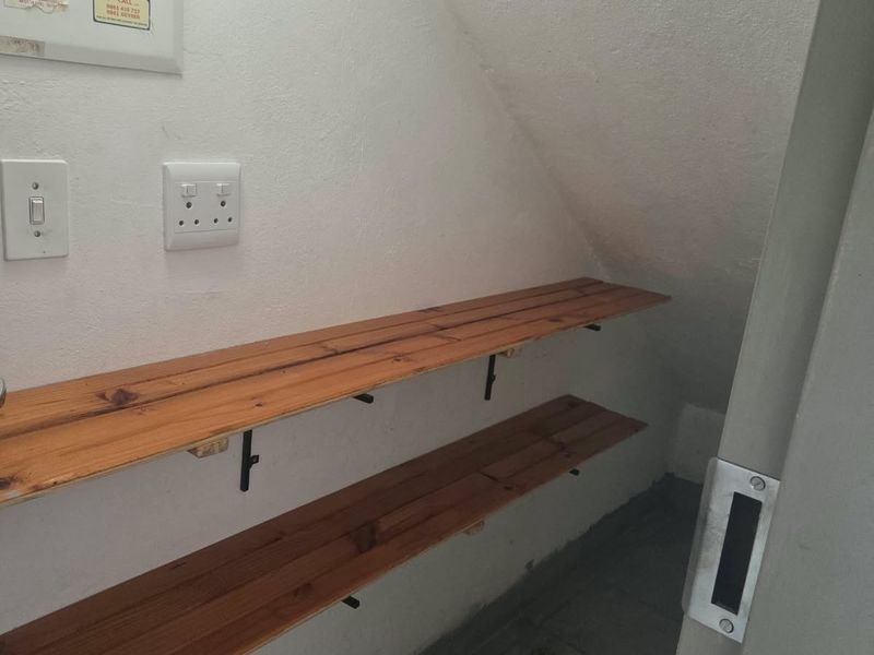 A compact utility storage space located under the stairs, featuring timber shelving, tiled flooring, and an integrated electrical distribution board.