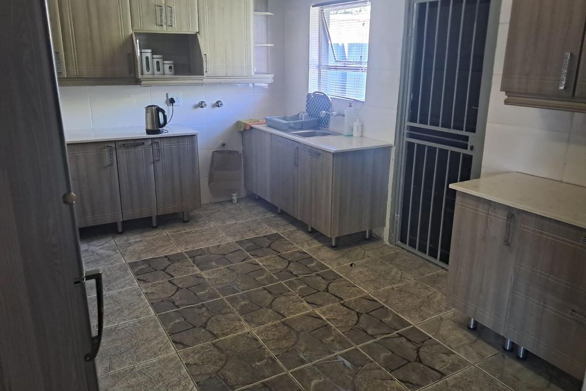 Functional kitchen featuring wood-look cabinetry, stone-effect countertops, tiled flooring, and a secure metal security gate leading to the exterior.