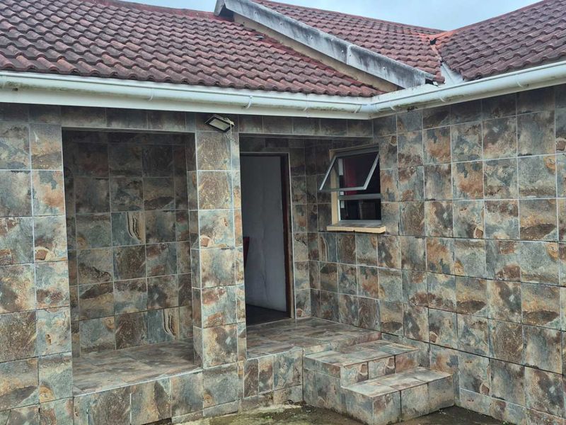 Rear exterior view of the house featuring a tiled facade, covered patio area with steps, and a pitched tiled roof with guttering.
