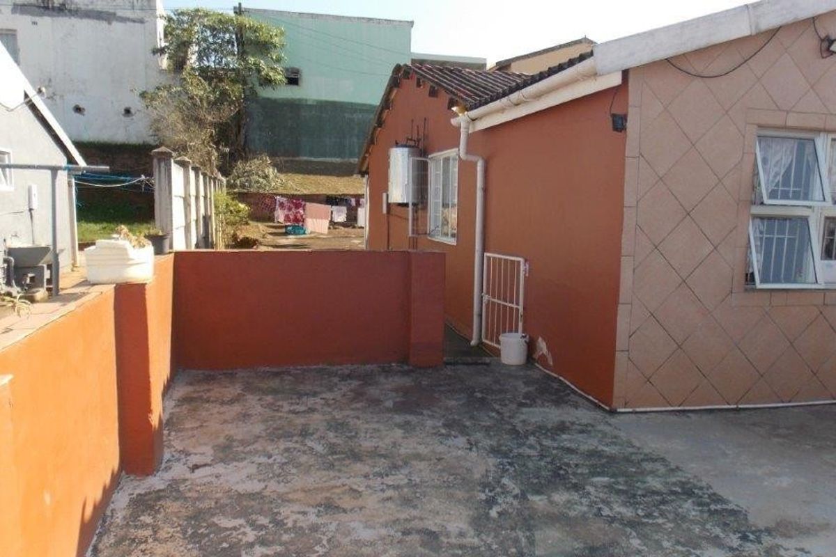 Rear exterior view of the property featuring a concrete patio area, boundary wall, and external geyser installation.