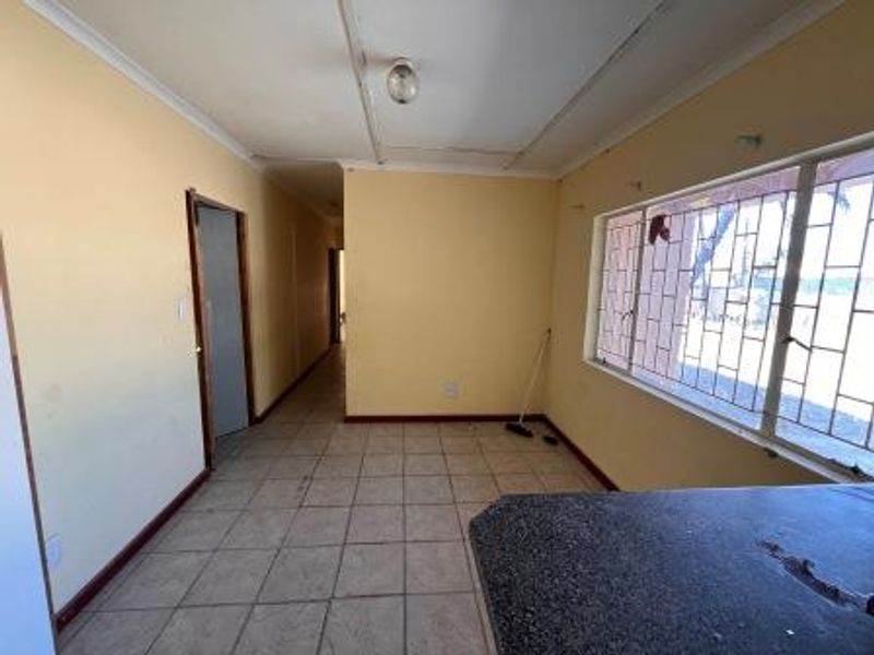 An open-plan living area featuring tiled flooring, security bars on windows, and a built-in counter, requiring cosmetic updates to improve its overall condition.