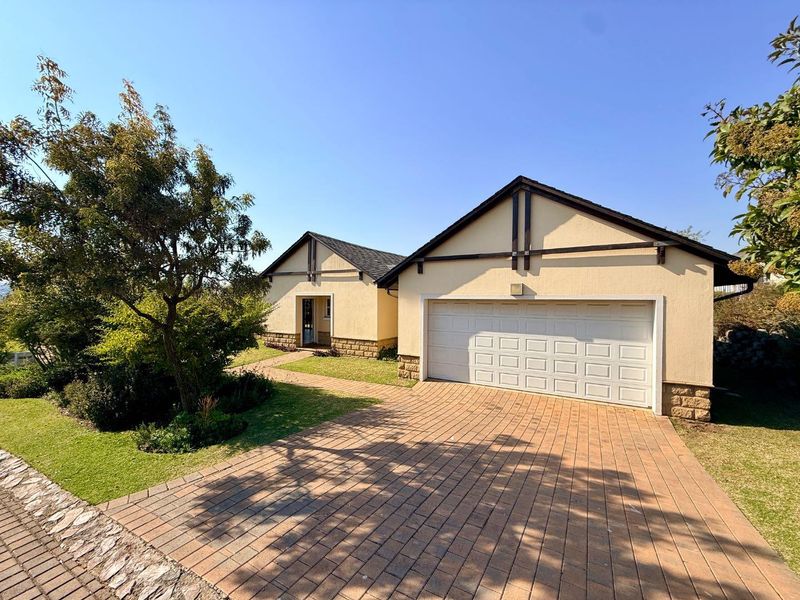 Front elevation of the property featuring a paved driveway, double garage, and well-maintained garden with stone-clad accents.