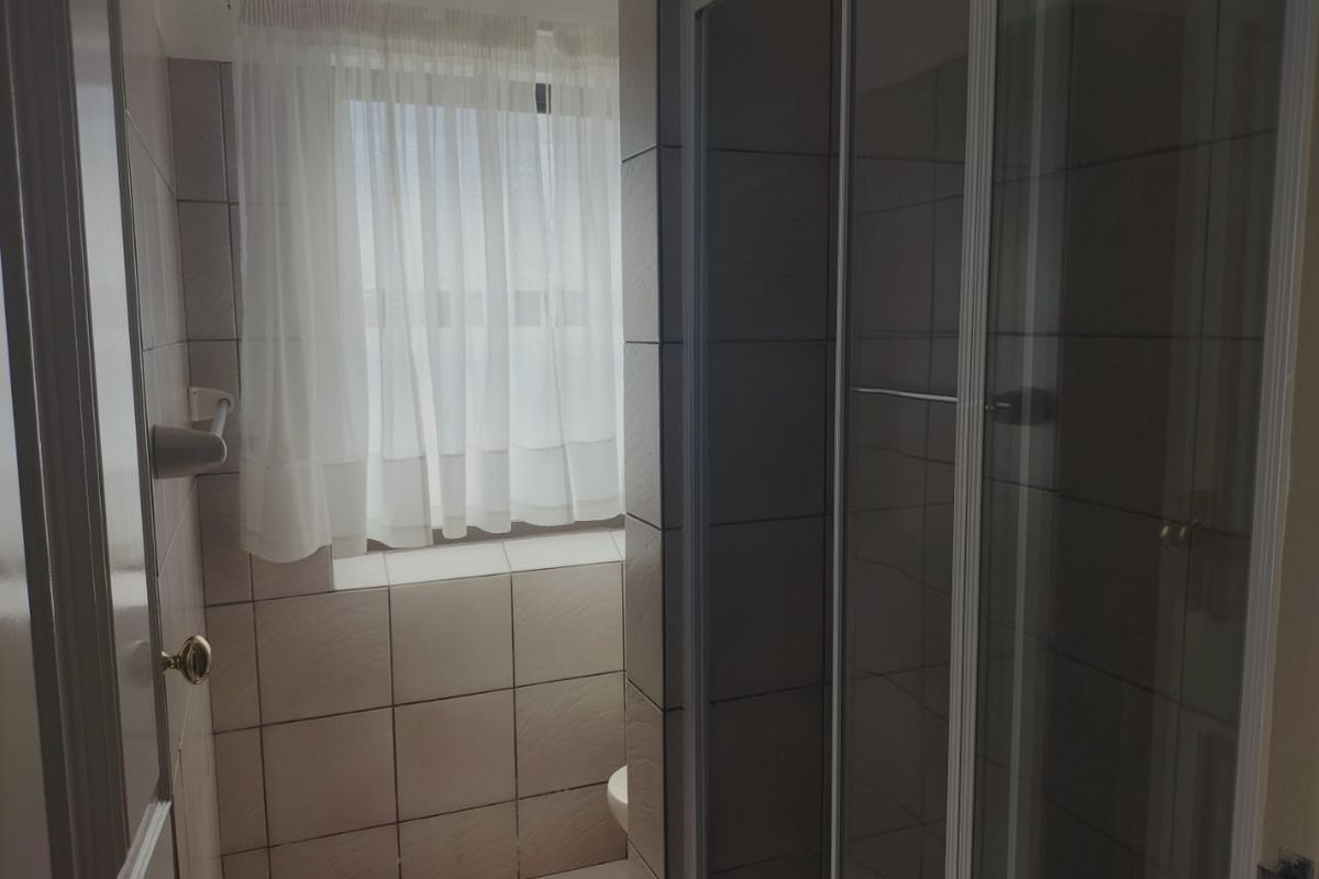 A functional bathroom featuring a glass-enclosed shower and neutral wall tiling.