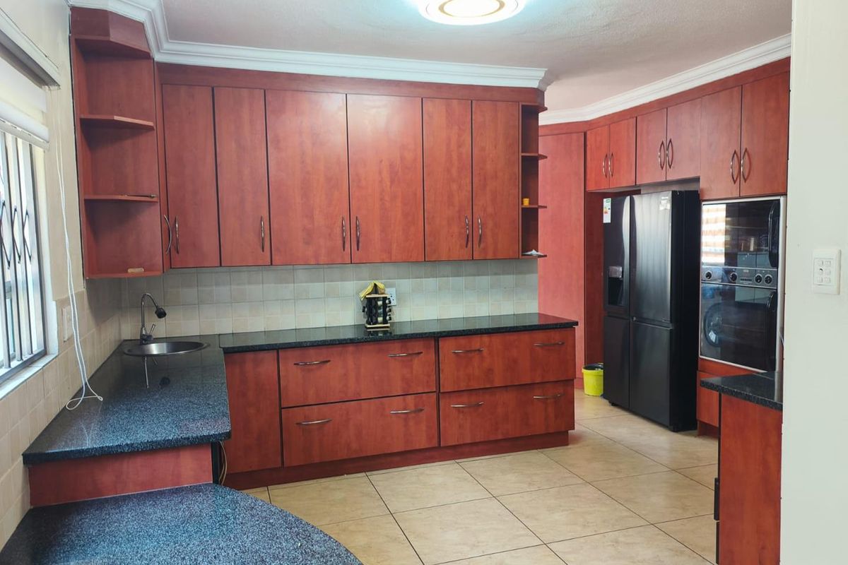 A functional kitchen featuring dark granite countertops, extensive wooden cabinetry, built-in oven, and tiled flooring with a classic cornice finish.