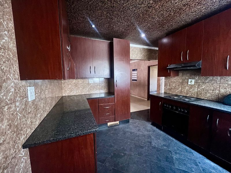 A functional kitchen featuring dark wood cabinetry, granite countertops, a built-in oven with hob, and tiled finishes throughout.