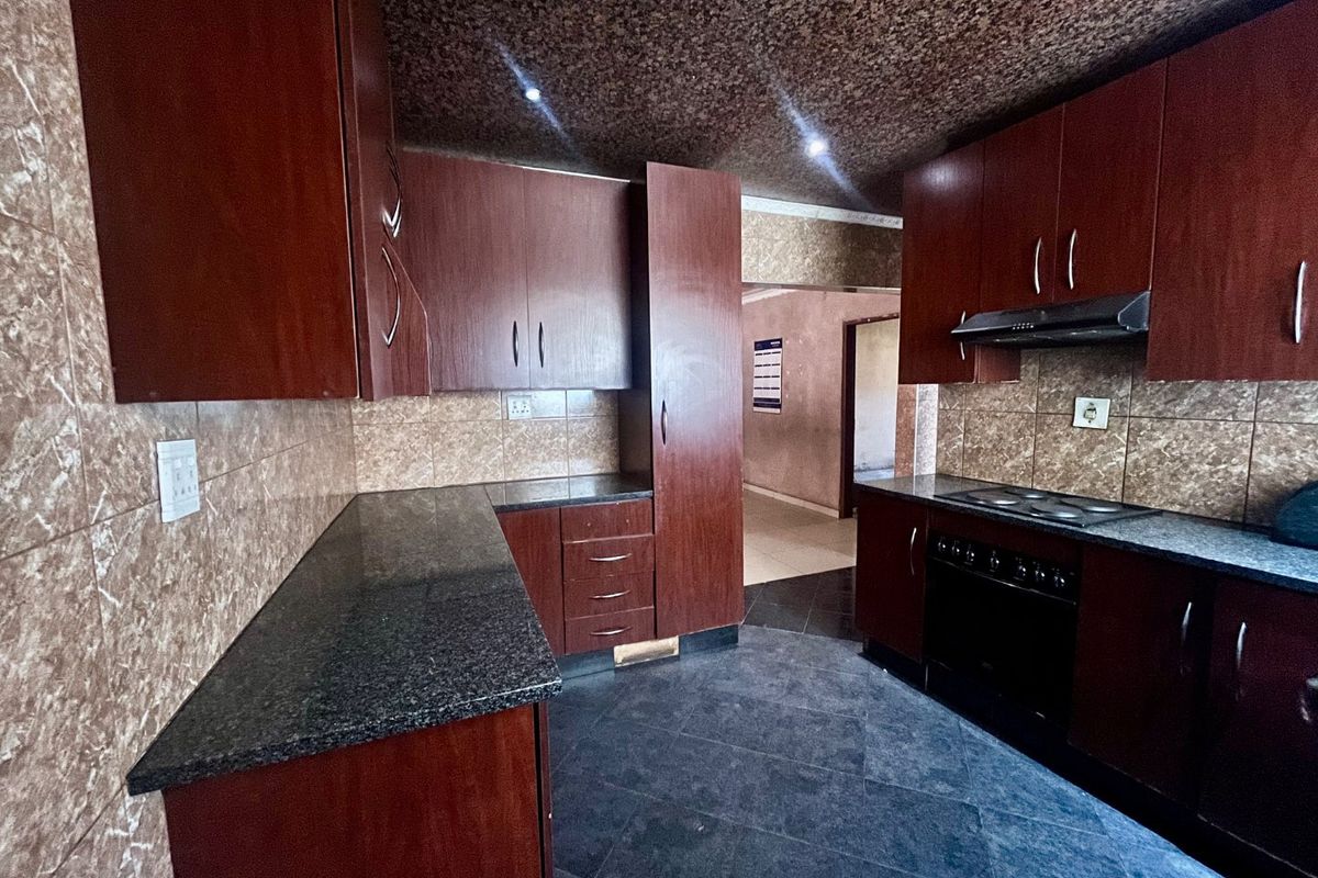 A functional kitchen featuring dark wood cabinetry, granite countertops, a built-in oven with hob, and tiled finishes throughout.