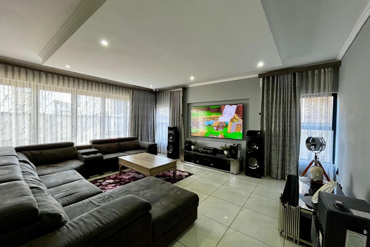 Spacious living room featuring large format floor tiles, recessed tray ceiling with downlighting, and expansive windows with floor-to-ceiling curtains.