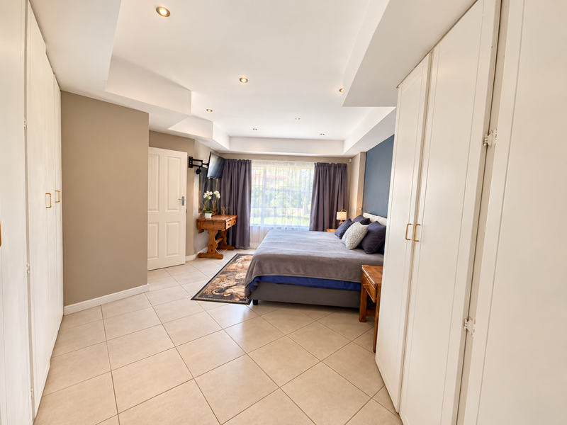 Spacious bedroom featuring extensive built-in cupboard storage, neutral tiled flooring, and a recessed ceiling with integrated downlighting.