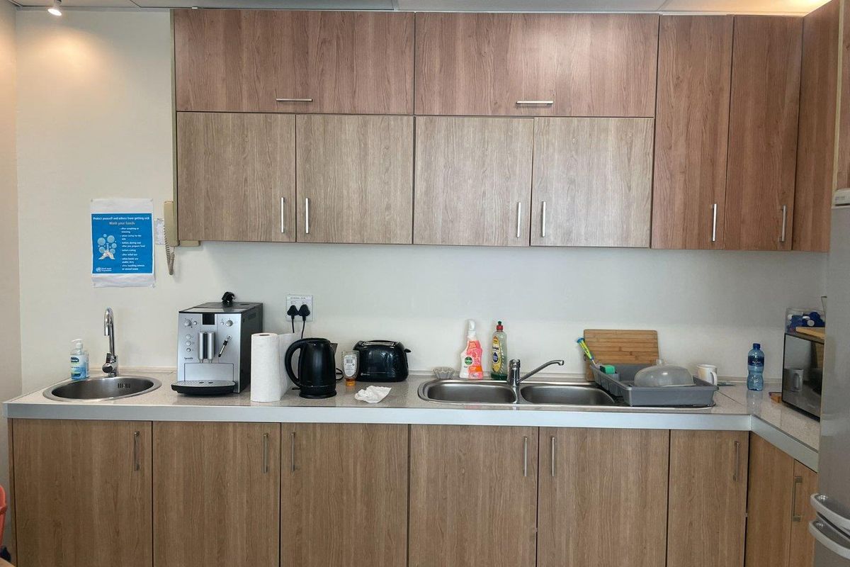 A functional office kitchenette featuring wood-grain cabinetry, dual stainless steel sinks, and laminate countertops, providing essential staff amenities.