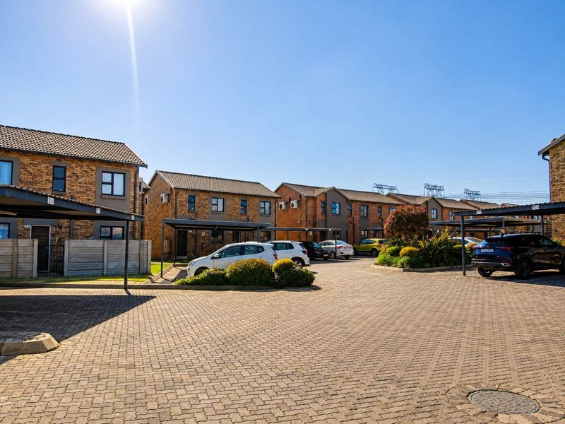 A view of the townhouse complex exterior featuring paved driveways, covered carports, and well-maintained facebrick residential units.