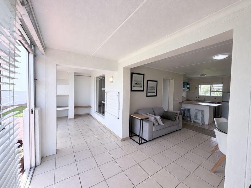 Bright open-plan living area featuring tiled floors, a functional kitchen with an island, and a seamless transition to an enclosed patio space.