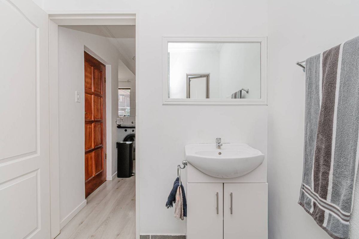 A clean, minimalist bathroom featuring a white vanity cabinet with a ceramic basin and a wall-mounted mirror, leading into an adjacent utility area.