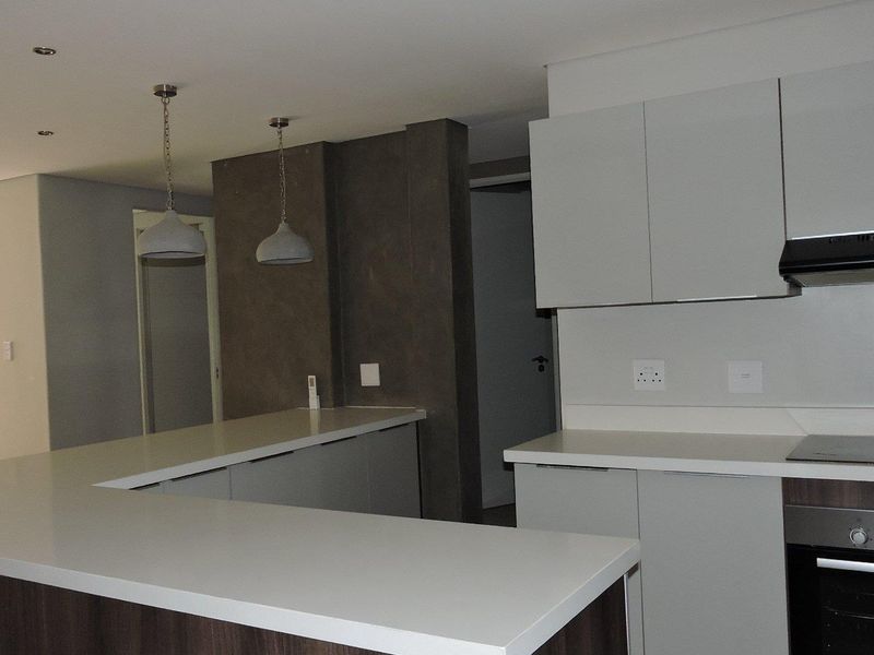 Modern kitchen featuring sleek cabinetry, stone countertops, integrated oven, and hob, complemented by contemporary pendant lighting and recessed ceiling lights.