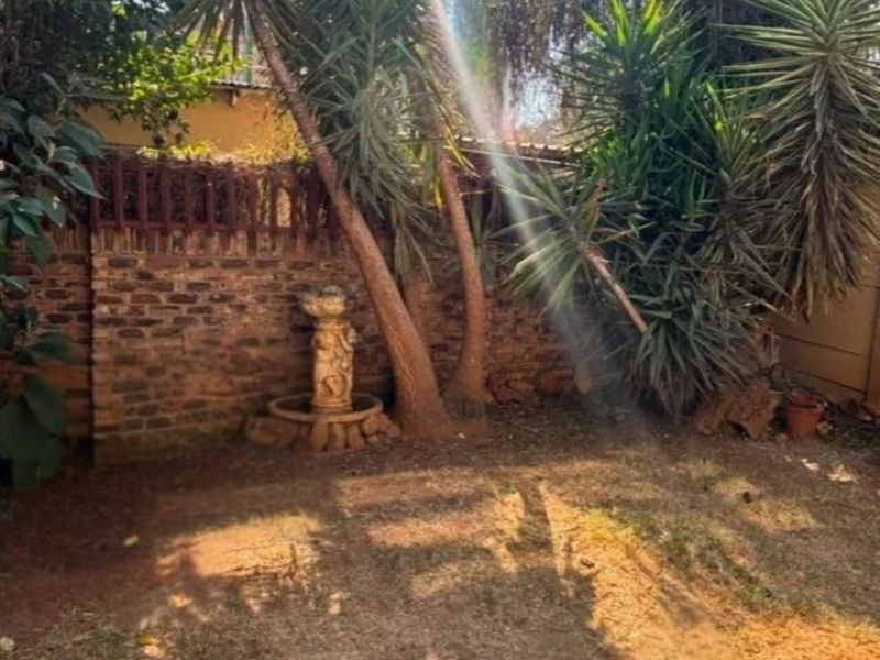 A private garden area featuring a brick boundary wall and a decorative stone fountain, surrounded by mature trees and shrubs.