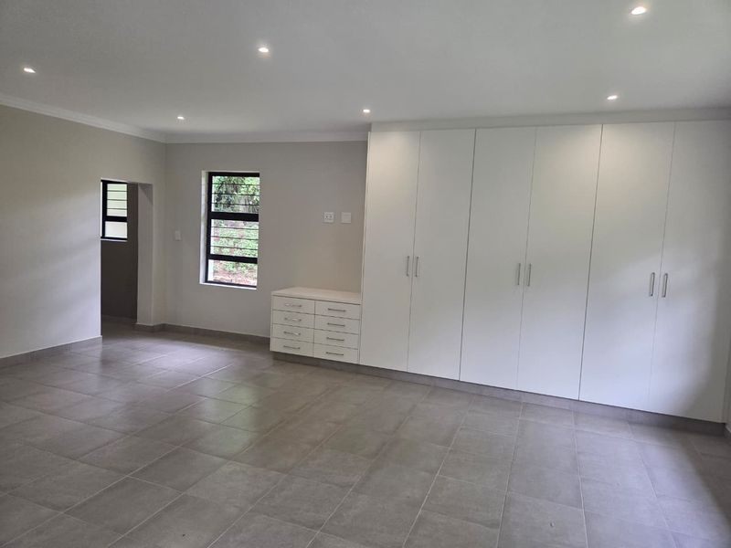 Spacious bedroom featuring neutral tiled flooring, extensive built-in cabinetry with integrated vanity, and modern recessed downlighting.