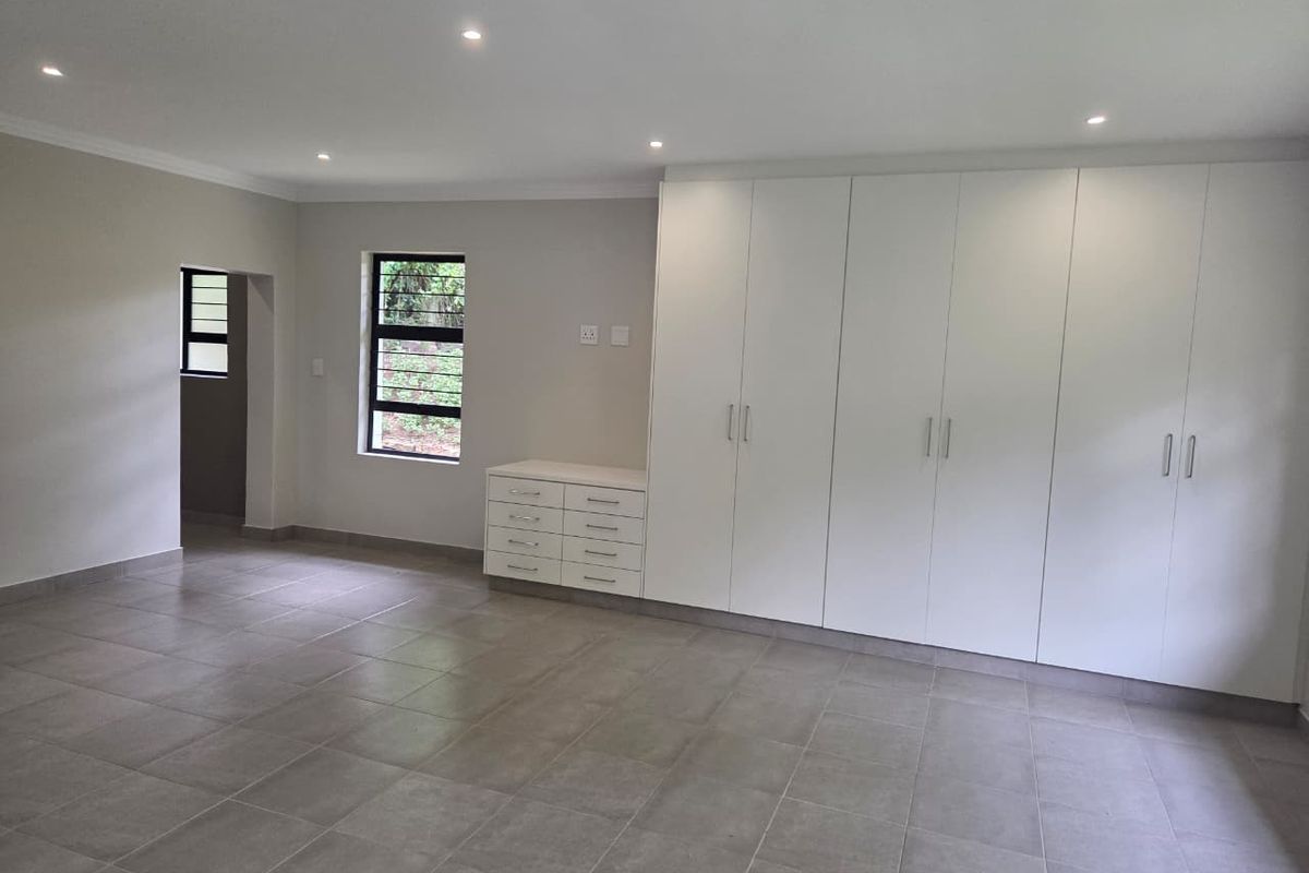 Spacious bedroom featuring neutral tiled flooring, extensive built-in cabinetry with integrated vanity, and modern recessed downlighting.
