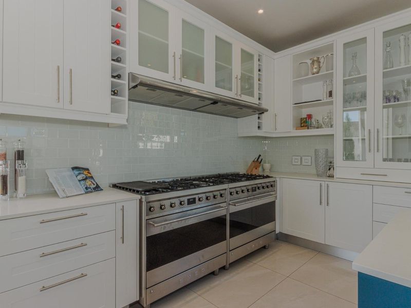 A modern, well-appointed kitchen featuring white cabinetry, stone countertops, a subway tile backsplash, and a professional-grade stainless steel double oven range.