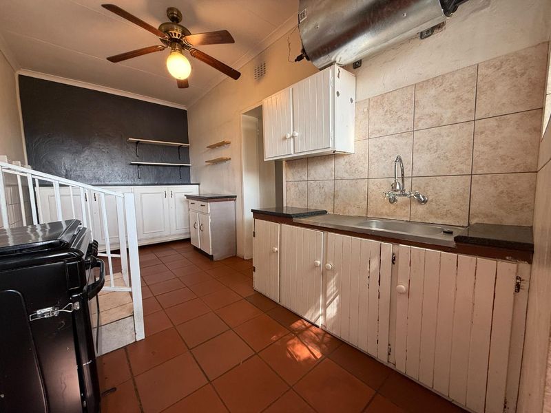 A functional scullery or utility area featuring built-in cabinetry, a stainless steel sink, terracotta flooring, and a ceiling fan.