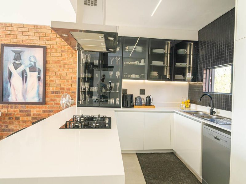 Modern kitchen featuring white cabinetry, quartz countertops, a gas hob with extractor, and a stylish exposed brick feature wall.