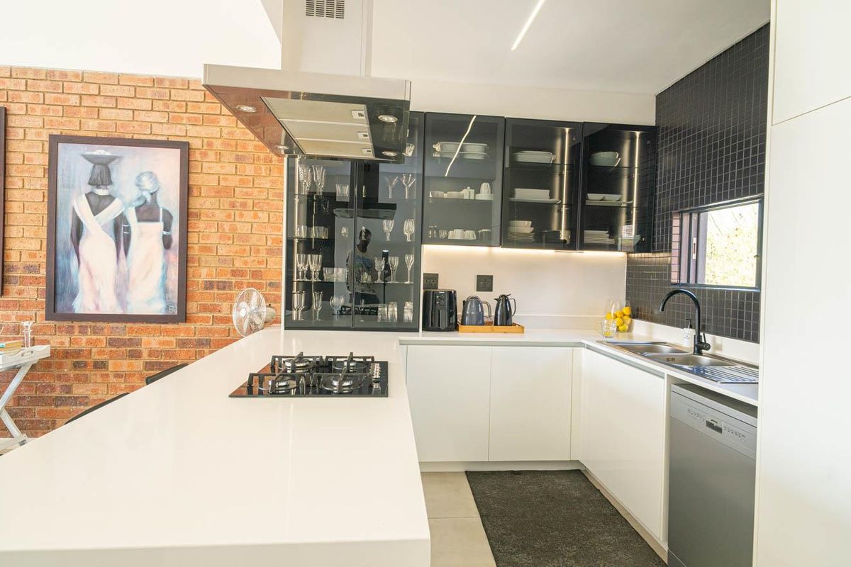 Modern kitchen featuring white cabinetry, quartz countertops, a gas hob with extractor, and a stylish exposed brick feature wall.