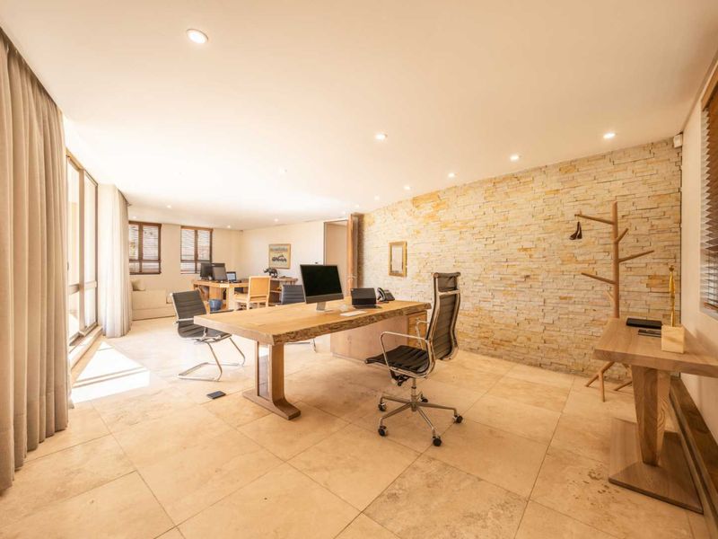 Spacious professional office featuring a natural stone accent wall, large format tiled flooring, and recessed lighting, creating a bright and modern workspace.