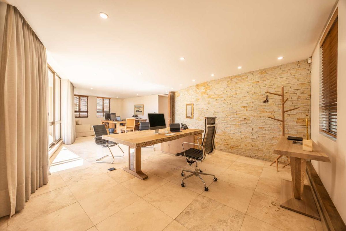 Spacious professional office featuring a natural stone accent wall, large format tiled flooring, and recessed lighting, creating a bright and modern workspace.