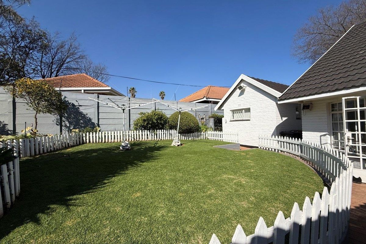 A well-maintained rear garden featuring a manicured lawn, white picket fencing, and a brick outbuilding under a tiled roof.