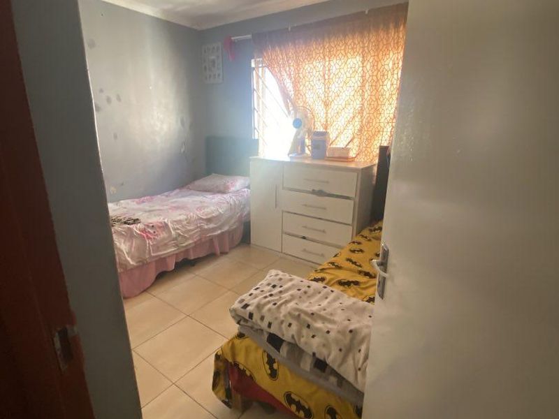 A compact bedroom featuring tiled flooring, security bars on the window, and coved ceilings, requiring cosmetic updates to the wall finishes.