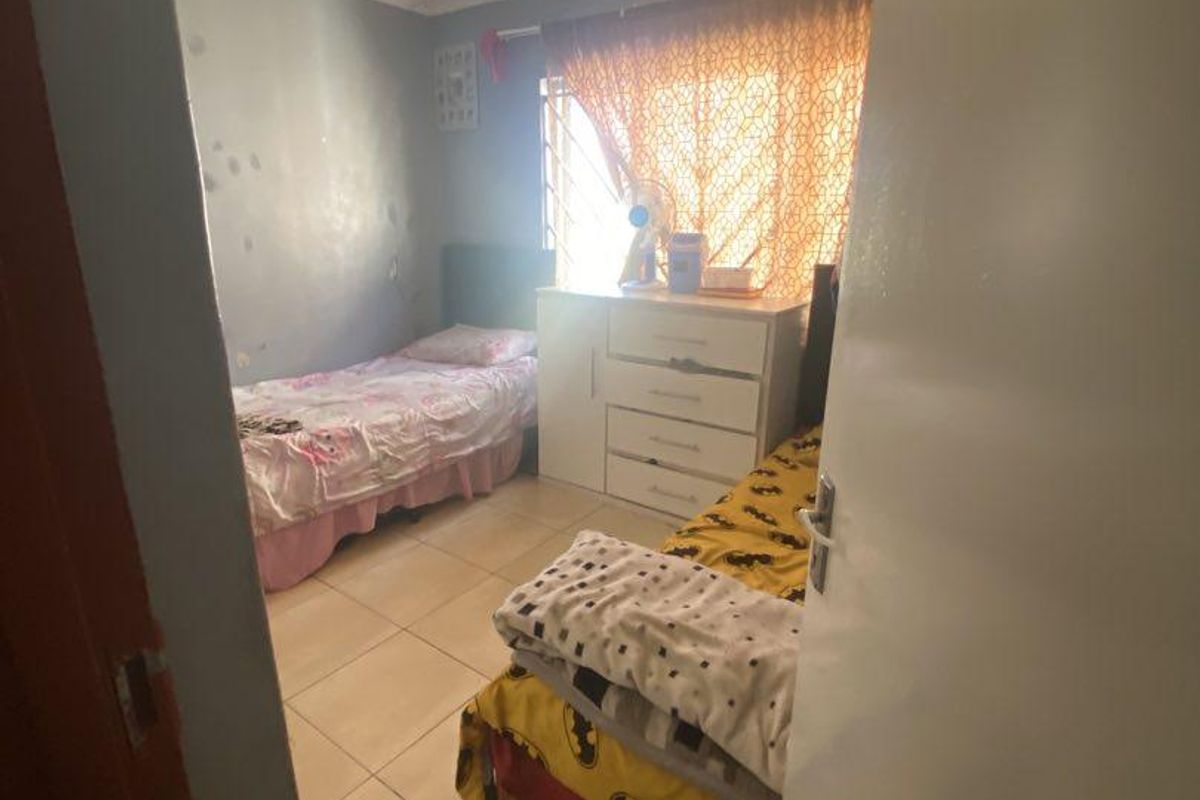 A compact bedroom featuring tiled flooring, security bars on the window, and coved ceilings, requiring cosmetic updates to the wall finishes.