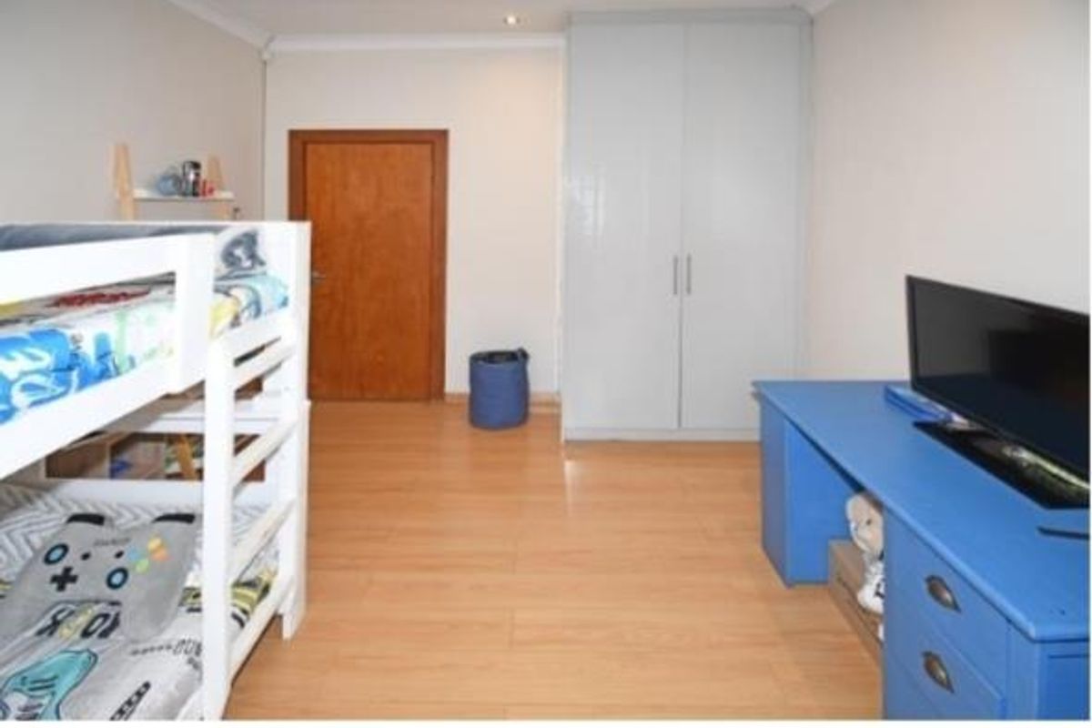 A functional bedroom featuring light-toned laminate flooring, a built-in wardrobe, and recessed ceiling lighting.