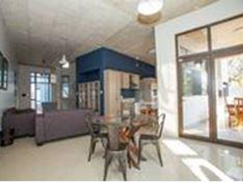 Spacious open-plan living and dining area featuring an exposed concrete ceiling, modern kitchen cabinetry, and large glass doors leading to an outdoor space.