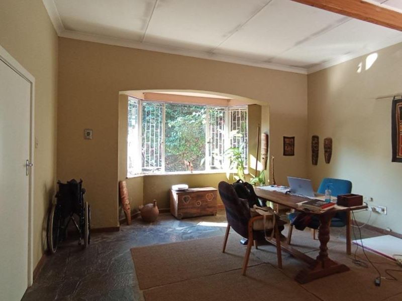 A living room featuring stone flooring, an exposed ceiling beam, and a large bay window that provides natural light.