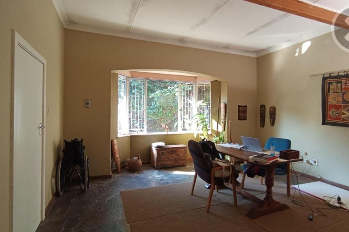 A living room featuring stone flooring, an exposed ceiling beam, and a large bay window that provides natural light.