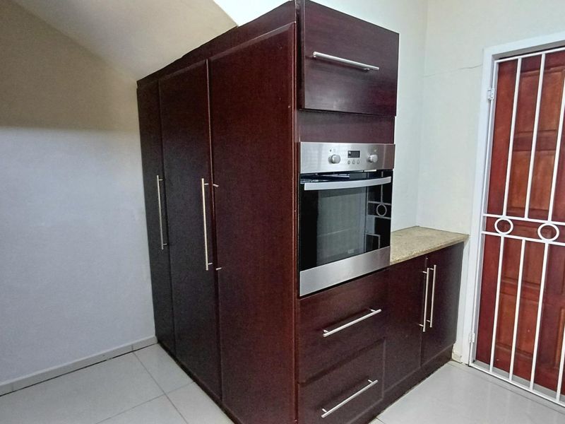 A kitchen area featuring dark wood built-in cabinetry, a stainless steel oven, and stone countertops, adjacent to a secure entrance door.