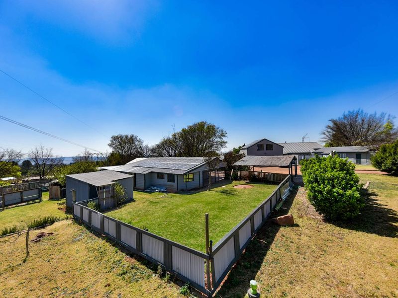 Aerial view of the property grounds featuring a fenced yard, solar panels on the roof, a carport, and a detached storage shed.