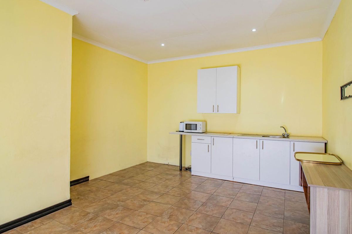 A functional kitchen area featuring white cabinetry, a built-in sink, and tiled flooring, offering a clean and simple layout.