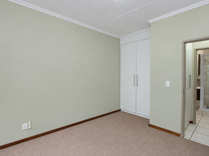 A clean, empty bedroom featuring neutral walls, carpeted flooring, and built-in cupboards, with direct access to an en-suite bathroom.