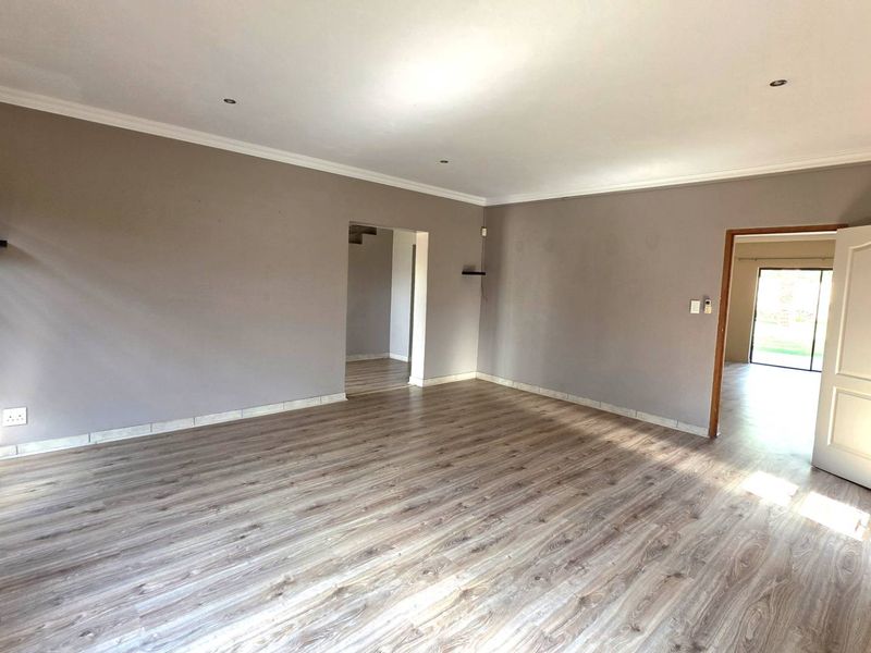 A spacious, empty living room featuring light-toned laminate flooring, neutral wall paint, and recessed ceiling lighting, offering a versatile blank canvas for interior design.