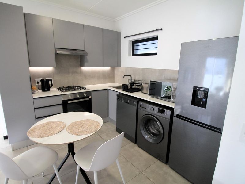 Modern kitchen featuring sleek grey cabinetry, gas hob, built-in oven, extractor fan, and integrated space for laundry appliances with neutral tiled flooring.